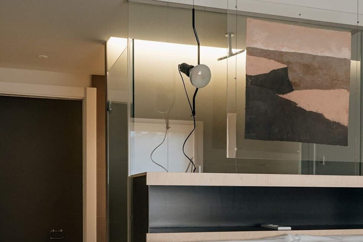 A modern hotel room with a large bed, a glass partition, and a wall-mounted artwork.