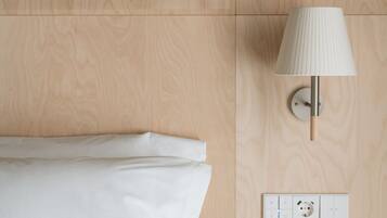 Een net opgemaakt bed met witte lakens, een wandlamp en een stopcontact op een houten wand.