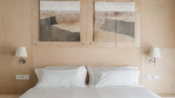 A hotel room with a wooden headboard, two wall-mounted lamps, a bed with white linens, and two abstract artwork pieces on the wall.