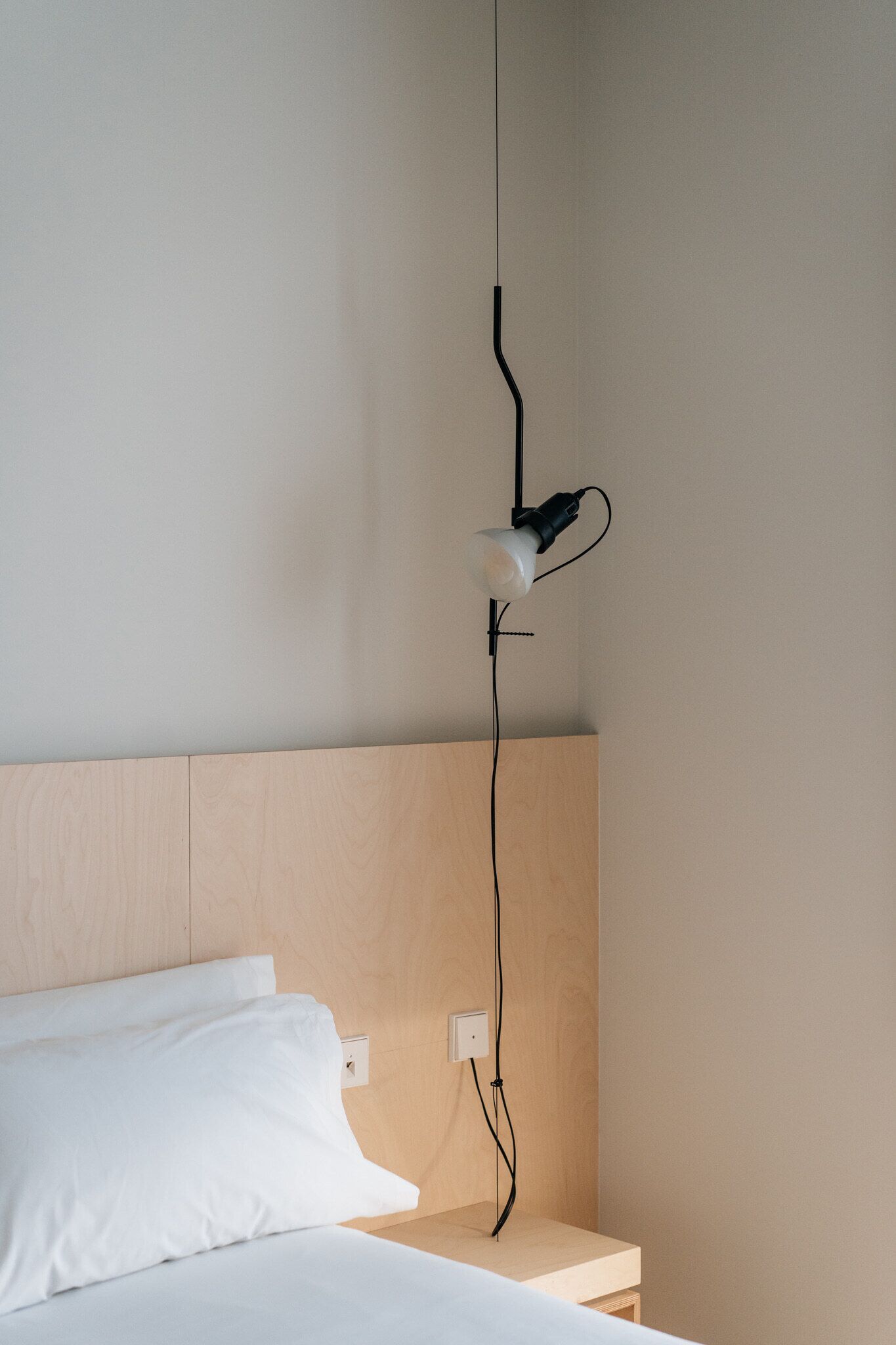 A minimalist bedroom with a wooden headboard, a bedside table, and a wall-mounted lamp.