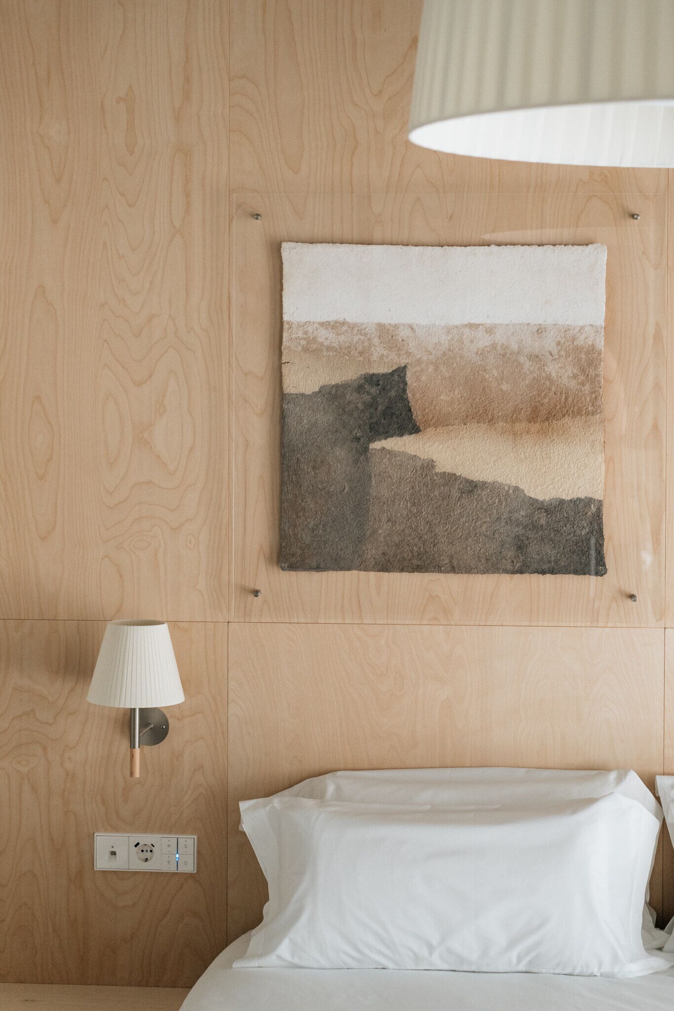 Habitación de hotel con pared de madera, un cuadro, una lámpara y una cama.
