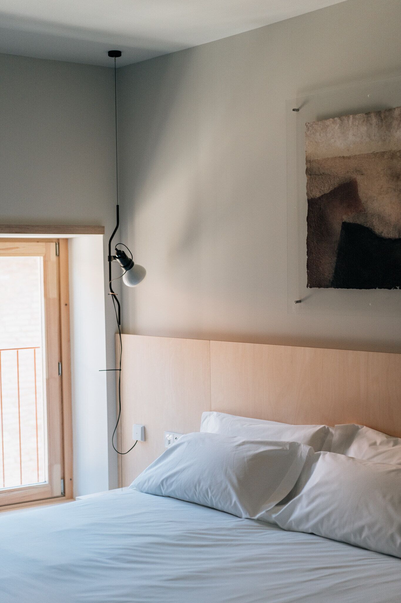 A bedroom with a bed, a wall-mounted lamp, a door, and a painting.