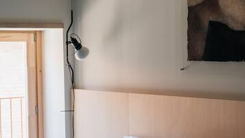 A bedroom with a bed, a wall-mounted lamp, a door, and a painting.
