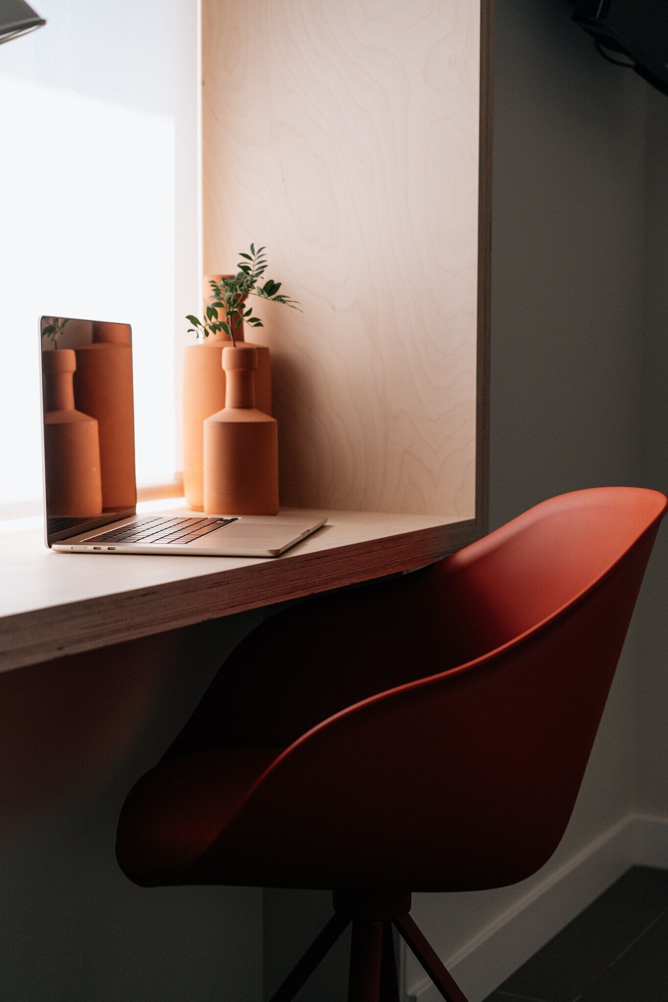 A modern workspace with a laptop on a wooden desk, a red chair, and decorative vases.