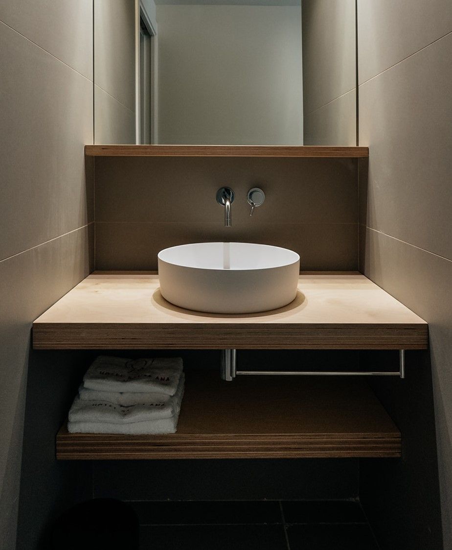 Une salle de bain moderne avec un lavabo rond, un miroir au-dessus et une étagère en bois en dessous.