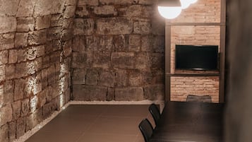 Ein Konferenzraum mit einem langen Tisch, Stühlen, einer Backsteinwand und einem an der Wand montierten Flachbildfernseher.