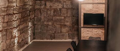 A conference room with a long table, chairs, a brick wall, and a flat-screen TV mounted on the wall.