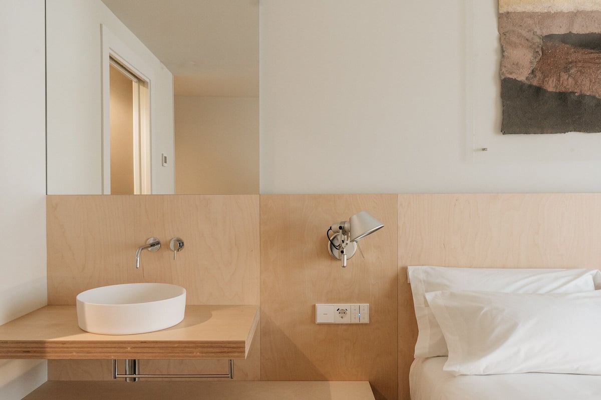 A modern bathroom with a wooden vanity, a white sink, and a wall-mounted light fixture.