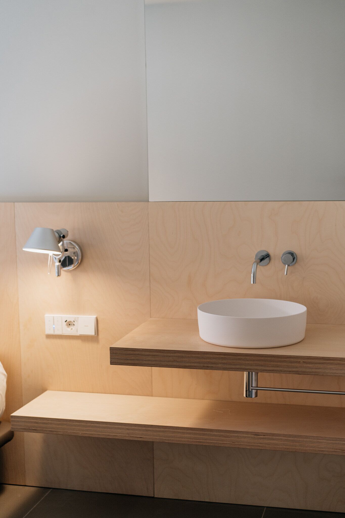 A modern bathroom with a round white sink, a wall-mounted light, and a wooden vanity.