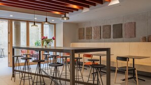 Zona de bar moderna con taburetes altos, una mesa central y una combinación de sillas rojas y negras.
