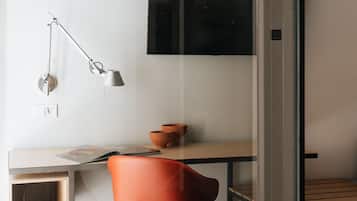 A modern office space with a desk, a red chair, a floor lamp, and a flat-screen TV mounted on the wall.