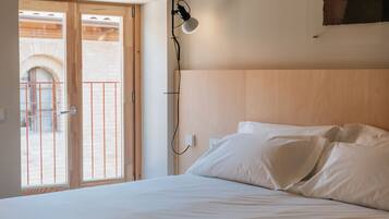 A bedroom with a bed, a wall-mounted lamp, and a view of an outdoor balcony with a railing.