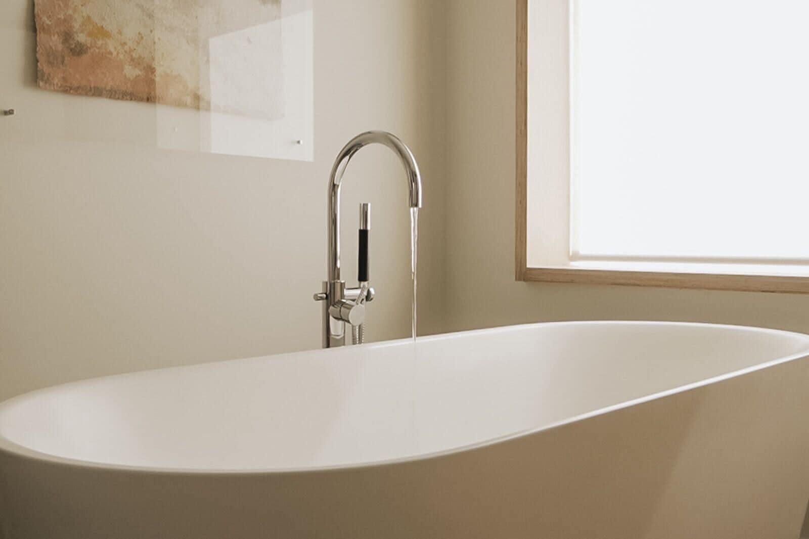 Une salle de bain moderne avec une baignoire sur pieds, un robinet mural et une fenêtre laissant entrer la lumière naturelle.