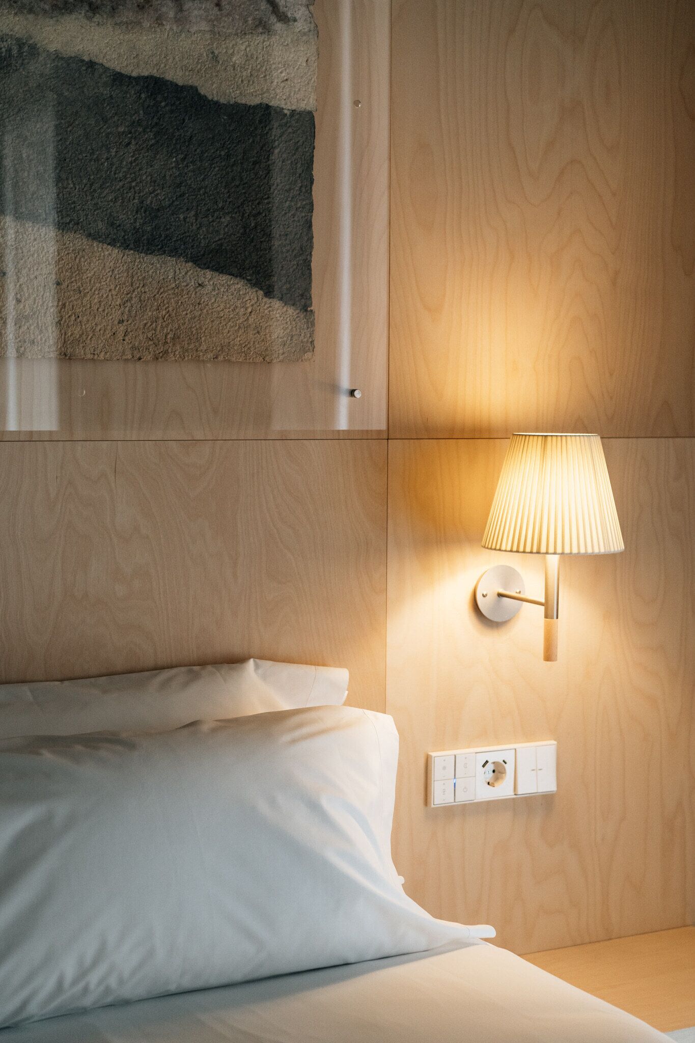 Habitación de hotel con una cama, una lámpara de pared y un panel de pared de madera.