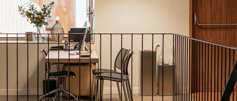 A modern office space with a desk, chairs, a large window, and a black pendant light.