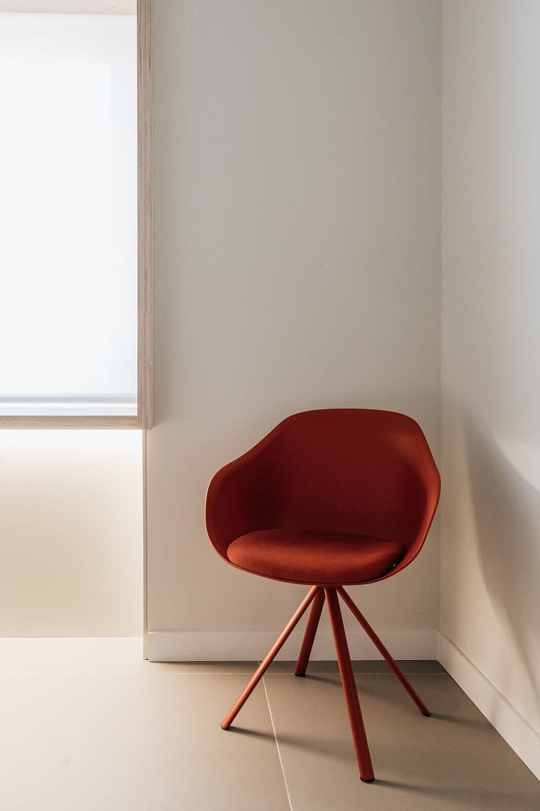 A modern chair with a unique design, positioned in a room with a large window and plain walls.