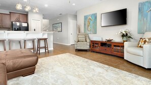Un salon moderne avec un canapé en cuir marron, un divan blanc, une table basse en bois et un téléviseur fixé au mur.