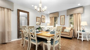 Un coin repas avec une table et des chaises en bois, un lustre et un canapé en arrière-plan.