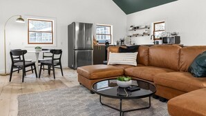 Un salon moderne avec un canapé en cuir marron, une table basse ronde et un coin repas comprenant une table blanche et des chaises noires.