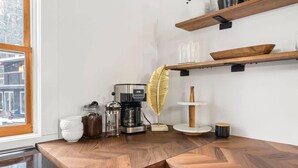 Une cuisine avec un plan de travail en bois, une machine à café, une bouilloire, un vase et une plume décorative.