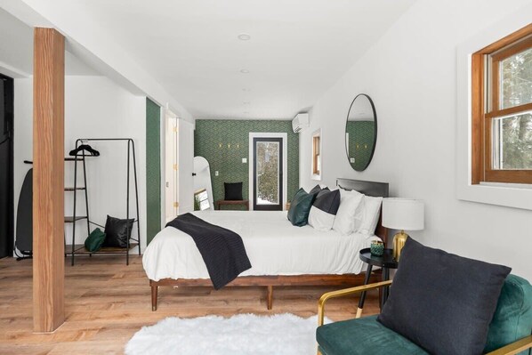 A modern bedroom with a bed, a chair, a mirror, and a window.