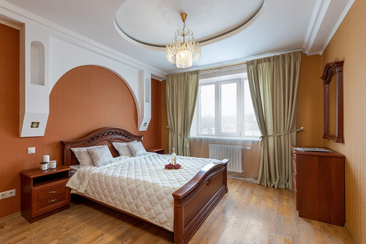A bedroom with a large bed, wooden headboard, a nightstand, a dresser, and a chandelier.