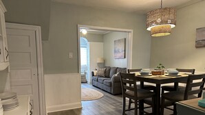 A dining area with a wooden table and chairs, a woven light fixture above, and a view into a living room with a sofa and a lamp. - Best Location in AC! Near Boardwalk, Casino Action (Atlantic City)
