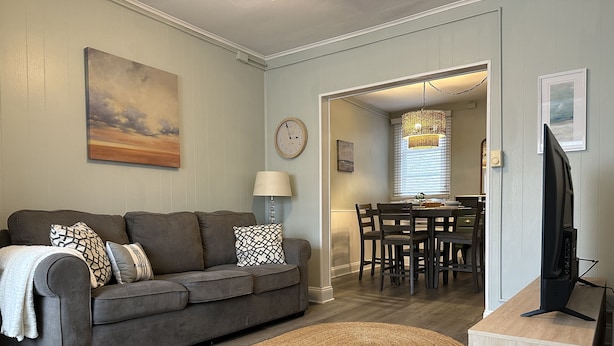 A living room with a grey sofa, a woven rug, a TV stand, and a dining area with a chandelier. - Best Location in AC! Near Boardwalk, Casino Action (Atlantic City)