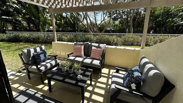 Un espace extérieur aménagé en patio, doté d’un coin salon couvert comprenant un canapé et des fauteuils, une petite table et des plantes en pot.