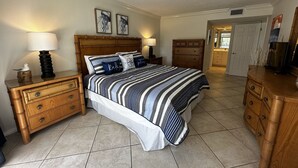 Une chambre à coucher avec un grand lit, des tables de chevet en bois, une commode et une porte donnant sur une autre pièce.