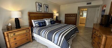 A bedroom with a large bed, wooden nightstands, a dresser, and a door leading to another room.