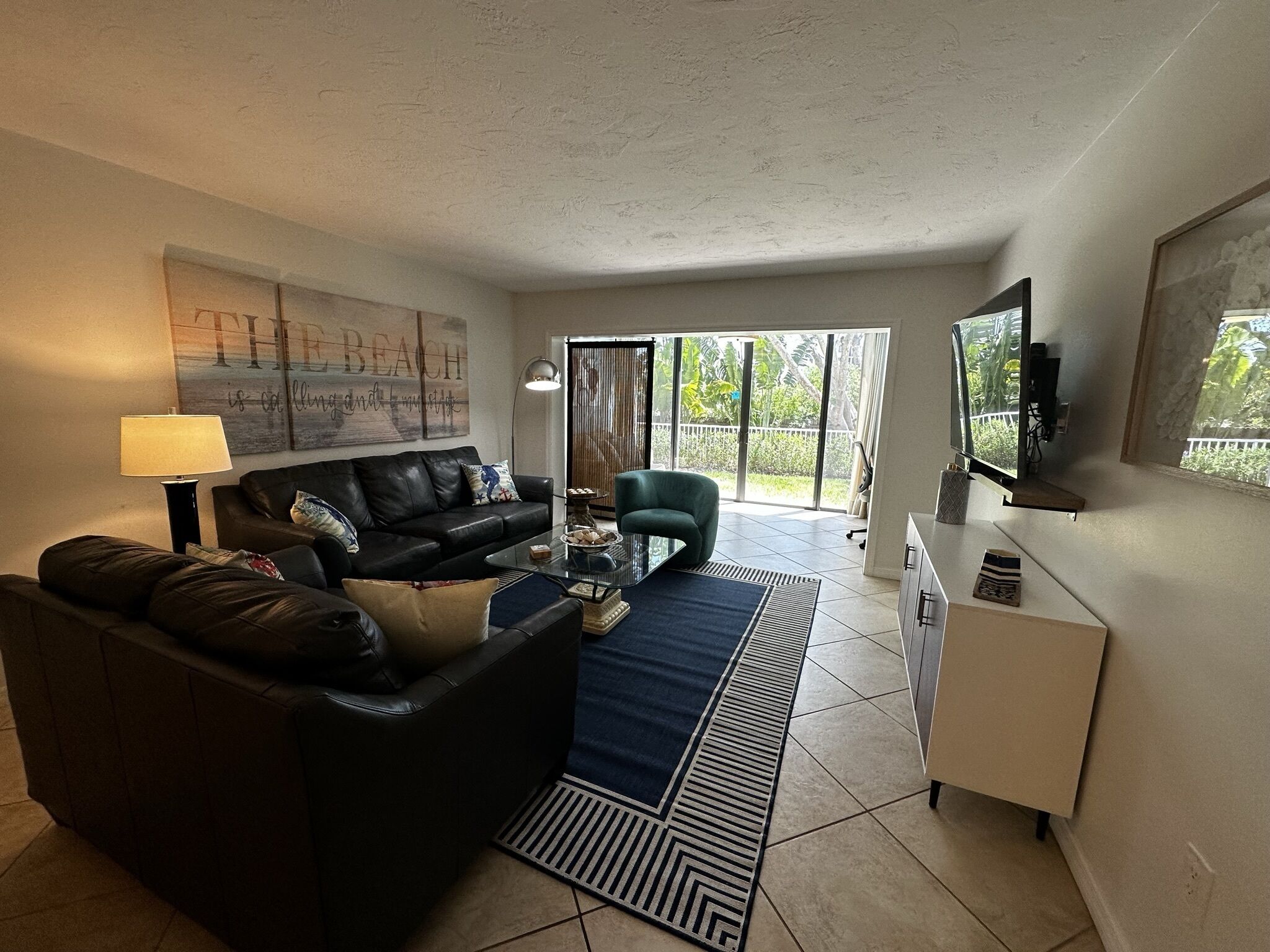 A living room with a black leather sofa, a glass coffee table, a blue rug, and a white cabinet.