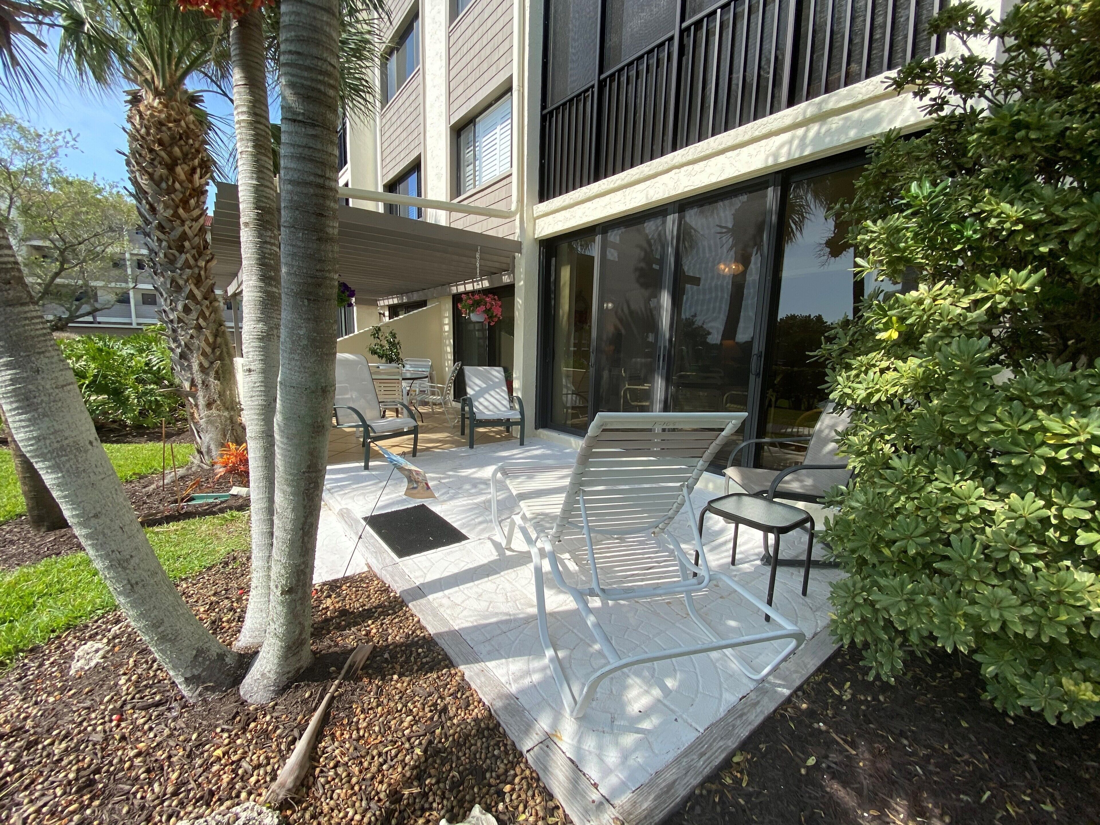 A modern outdoor patio with seating, a pergola, and a view of a building with large windows.