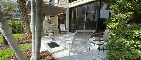 A modern outdoor patio with seating, a pergola, and a view of a building with large windows.