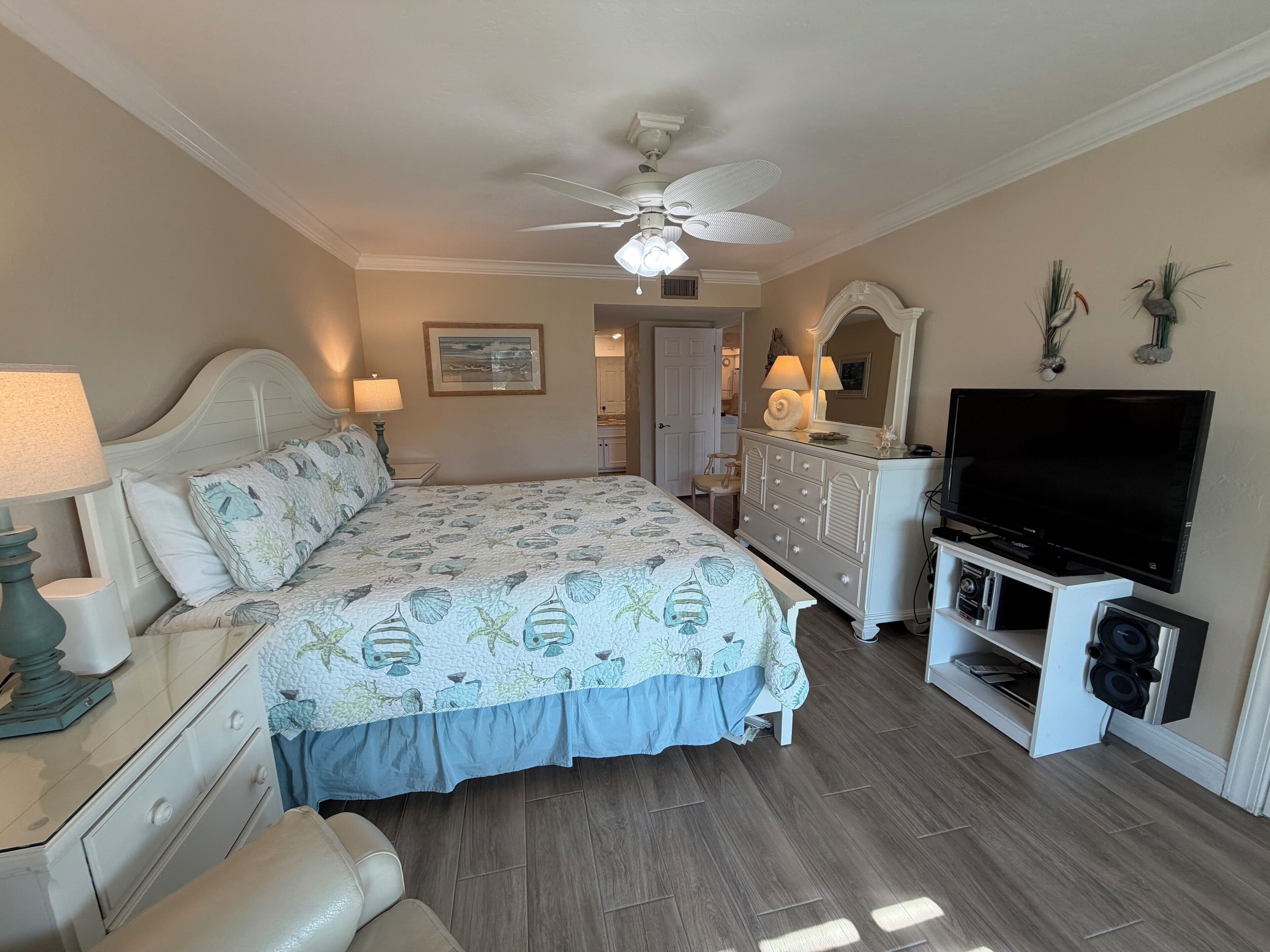 Een slaapkamer met een bed, bedlampen, een dressoir, een televisie en een plafondventilator.