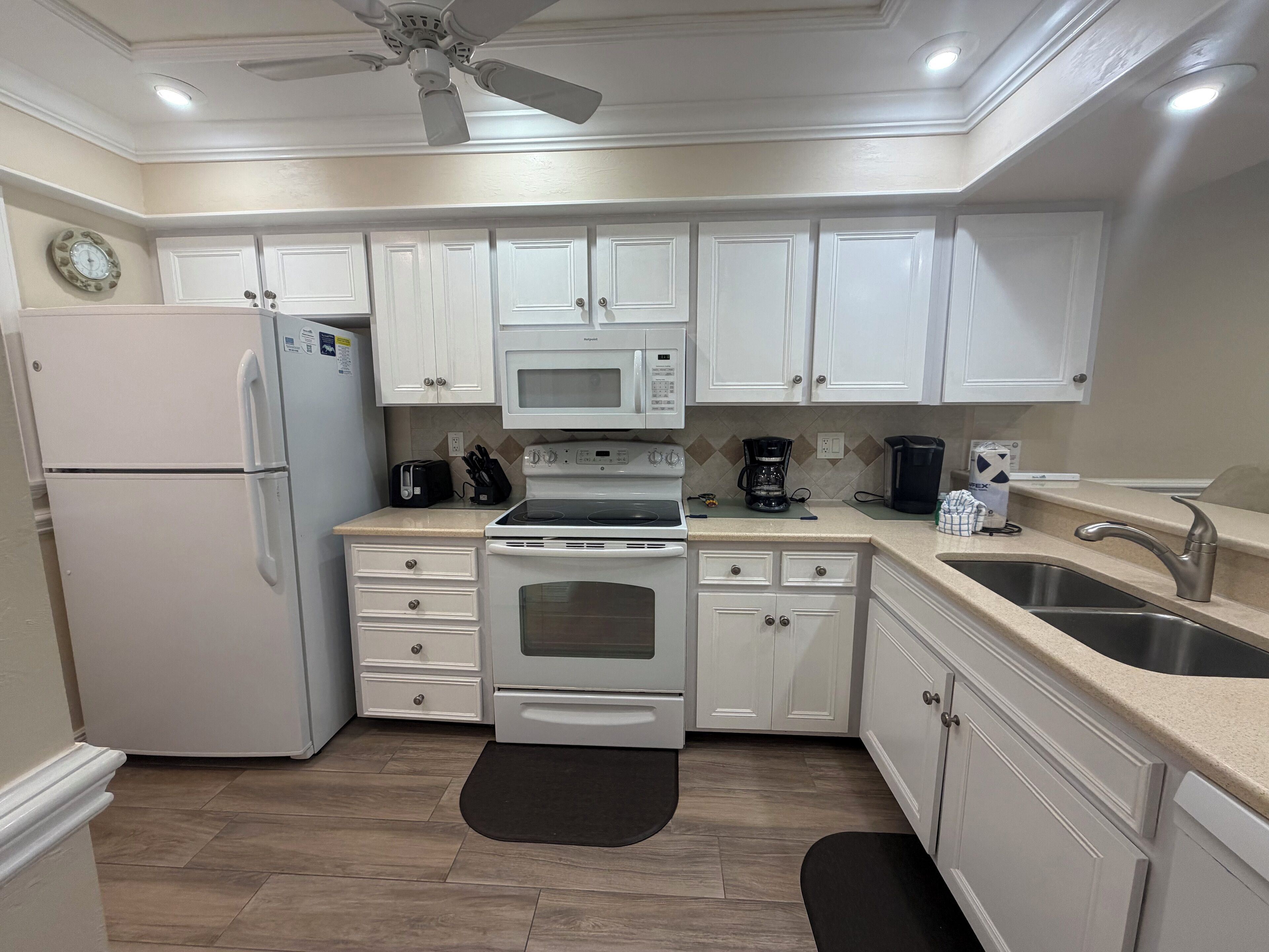 A modern kitchen with white cabinets, a refrigerator, an oven, a microwave, a coffee maker, and a sink.