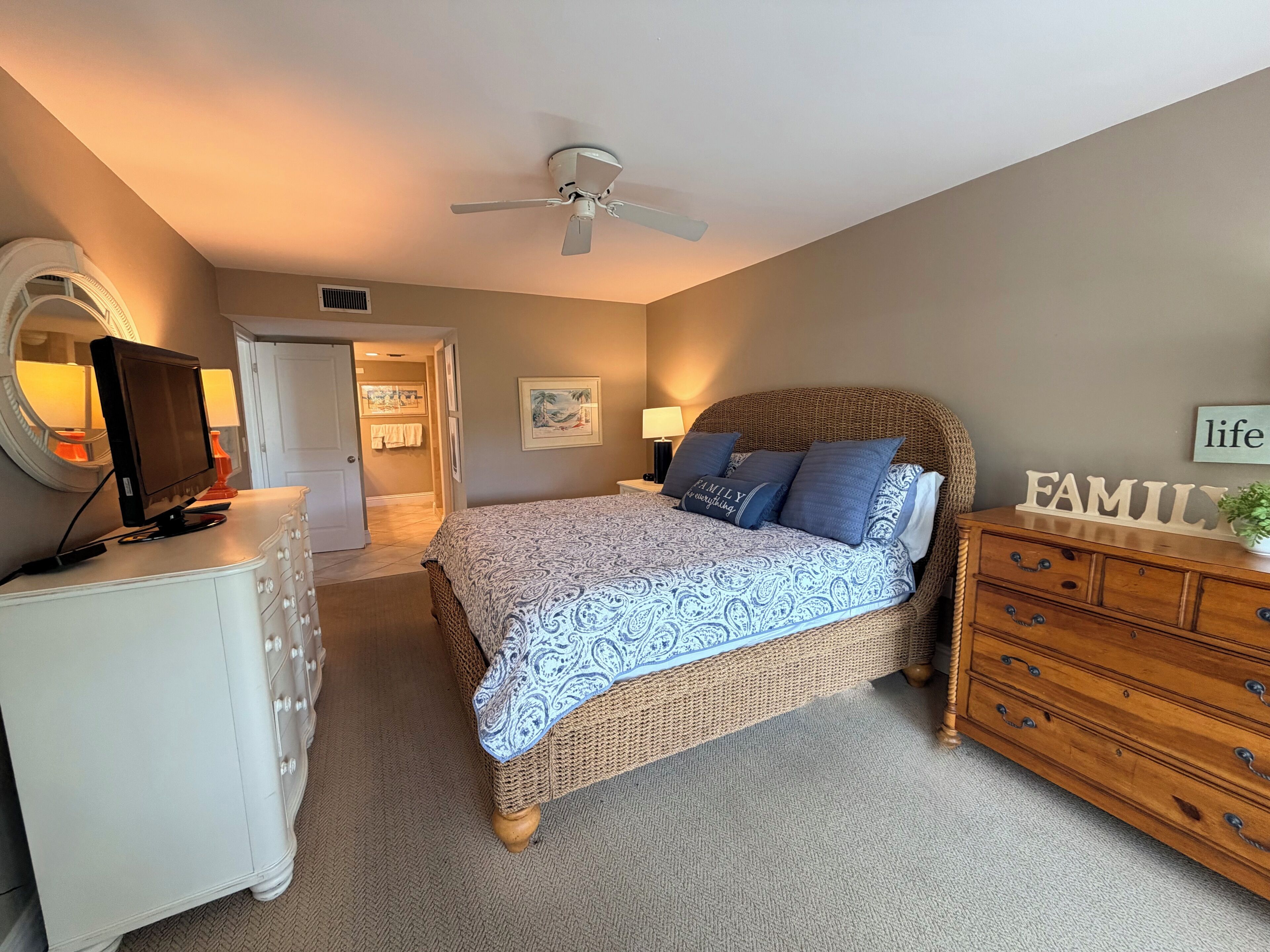 A bedroom with a bed, dresser, TV, and ceiling fan.