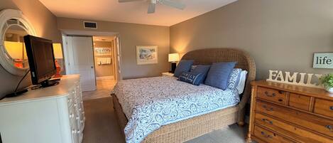 Un dormitorio con cama, cómoda, televisor y ventilador de techo.