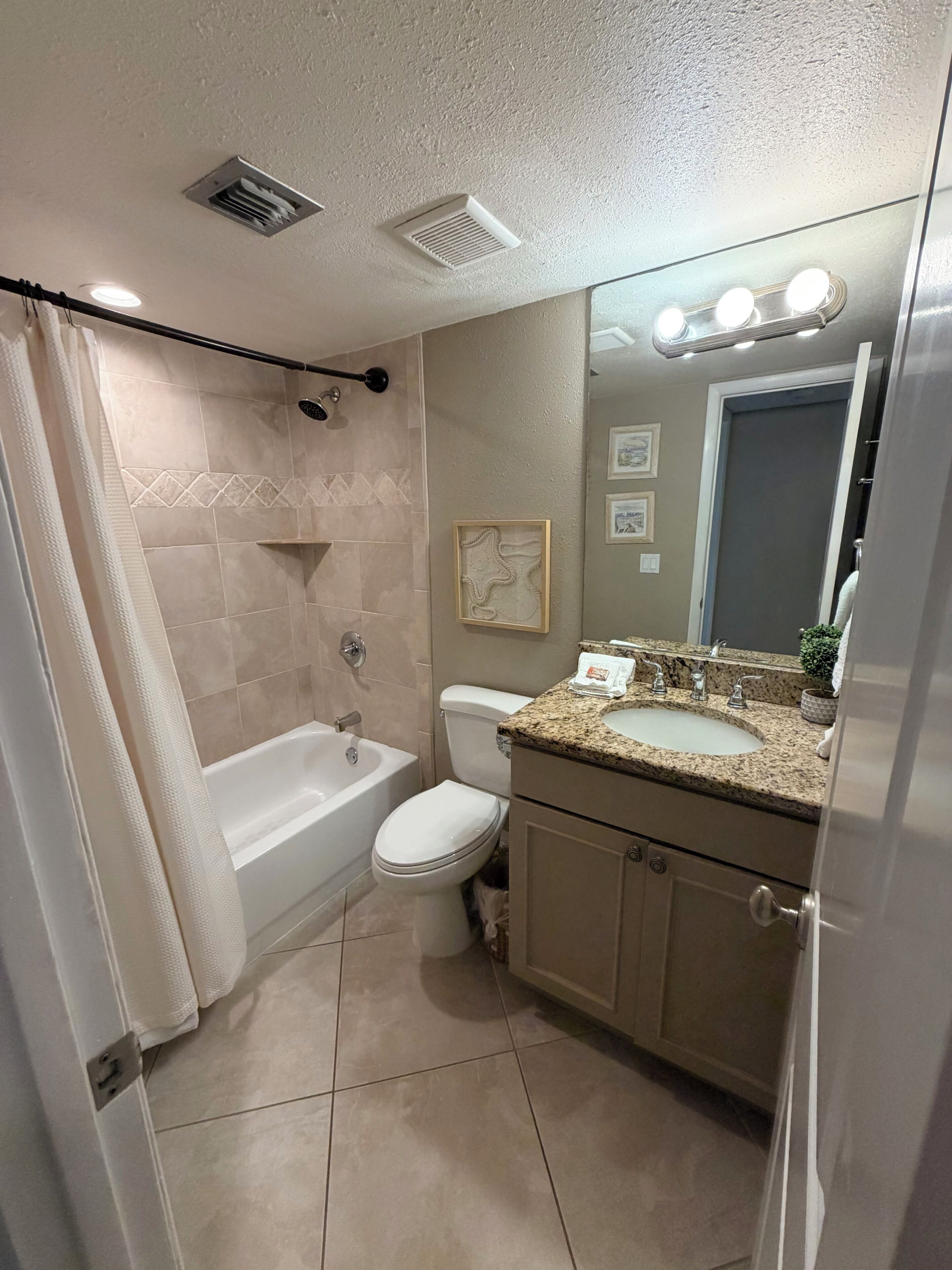 A bathroom with a bathtub, toilet, vanity with a sink, and a mirror with lights.