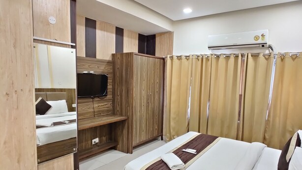 A modern hotel room with a wooden bed frame, a built-in wardrobe, a flat-screen TV, and a ceiling fan. - Hotel Raj Darbar (Amritsar)
