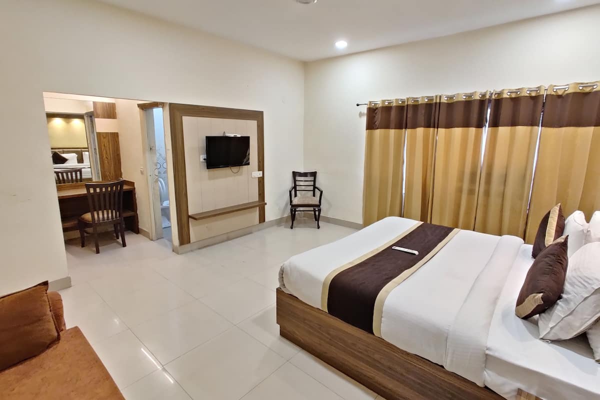 A hotel room with a bed, a desk, a chair, a television, and a bathroom visible through an open door.