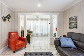 Un salon moderne avec un fauteuil en cuir rouge, un canapé en cuir noir agrémenté d’un coussin bleu, et un mur décoratif en bois sur lequel est inscrite une citation inspirante.