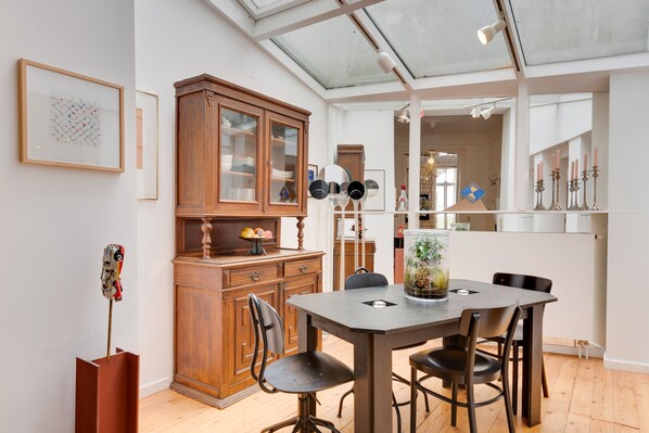 A dining area with a wooden cabinet, a table with chairs, and a glass vase with plants. - Saint Catherine Art Residence (Brussels)