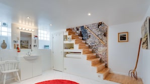 Une salle de bain moderne avec un meuble-lavabo blanc, un tapis rouge et un escalier en bois avec un mur en briques.