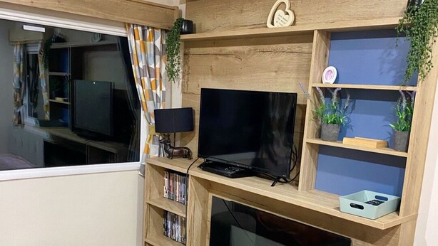 Una sala de estar con televisor, chimenea, estantes de madera y un ventanal con cortinas.