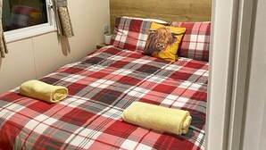 Un dormitorio con una colcha escocesa, dos cuadros en la pared y una ventana con cortinas.