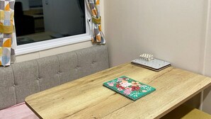 Una habitación con ventana, un banco tapizado en gris, una mesa de madera y una libreta.