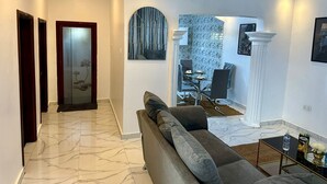 Een moderne woonkamer met een marmeren vloer, een bank, een glazen salontafel en een eethoek met behang met een patroon.