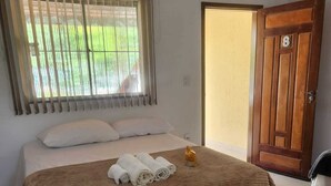 Ein Hotelzimmer mit Bett, einem Fenster mit Jalousien, einer Tür und Blick auf Grünfläche.