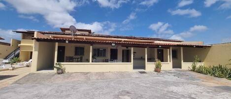 Un edificio de dos pisos con techo de tejas, antena parabólica y un patio cubierto con plantas en macetas.